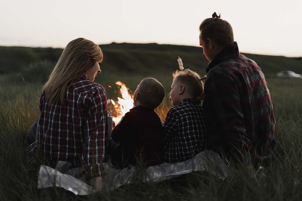 A family of four people, dad, mom and two sons are sitting around the fire.